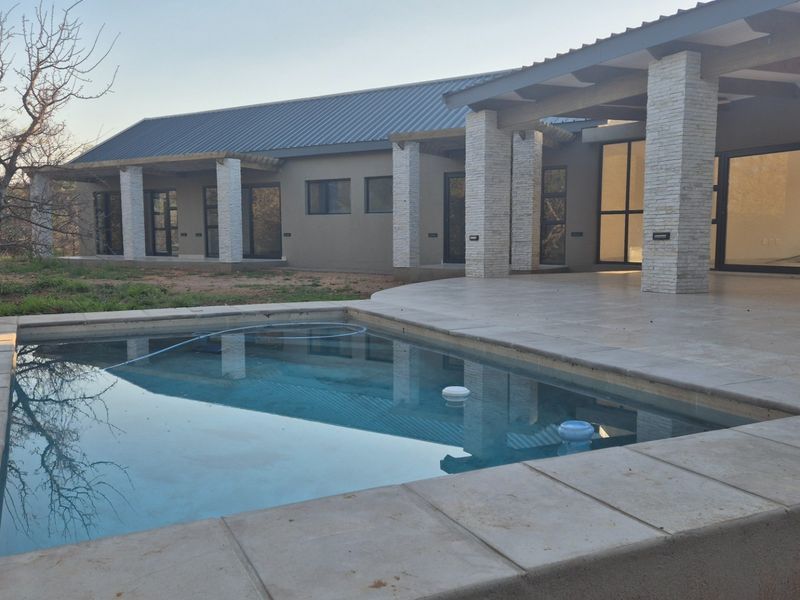 A modern home exterior featuring a swimming pool, stone-clad pillars, and a spacious covered patio area with large sliding glass doors.