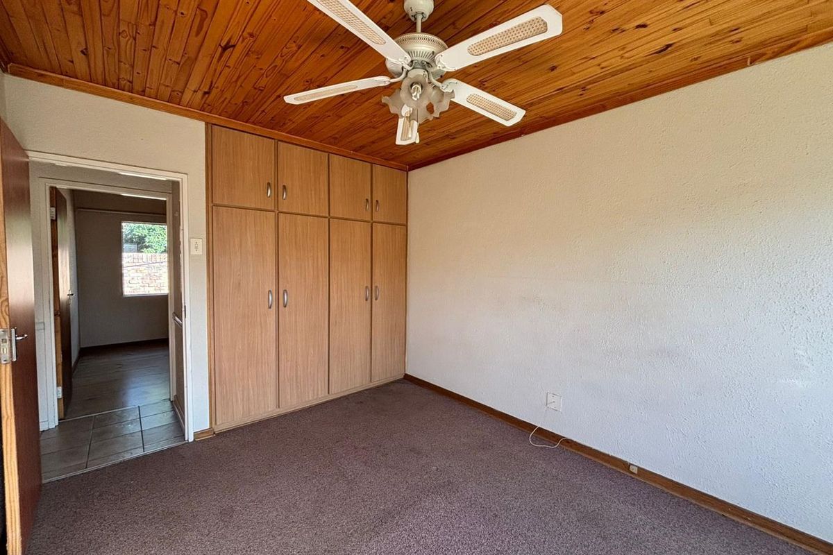 A bedroom featuring built-in wooden cupboards, a timber-clad ceiling with a central fan, and carpeted flooring.