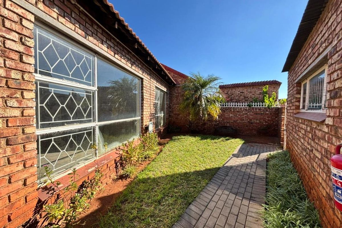A private rear courtyard featuring a brick-paved walkway, a small lawn area, and perimeter brick walls, providing a low-maintenance outdoor space.