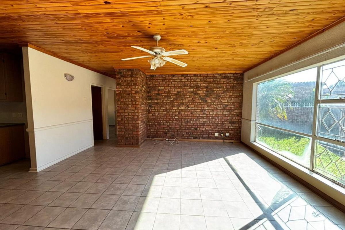 Spacious living area featuring a rustic exposed brick feature wall, timber-clad ceiling with a fan, and large windows providing ample natural light.