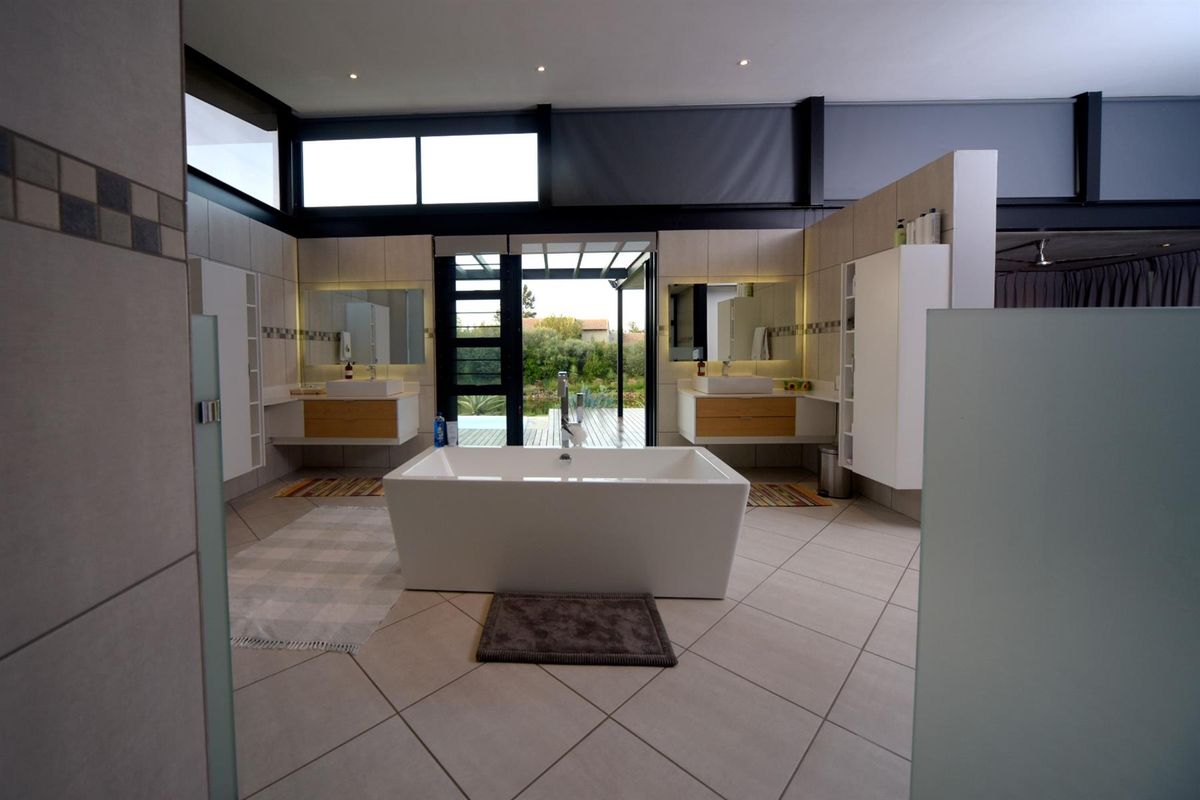 Spacious modern bathroom featuring a central freestanding bathtub, dual floating vanities with integrated sinks, and large windows providing natural light and outdoor access.