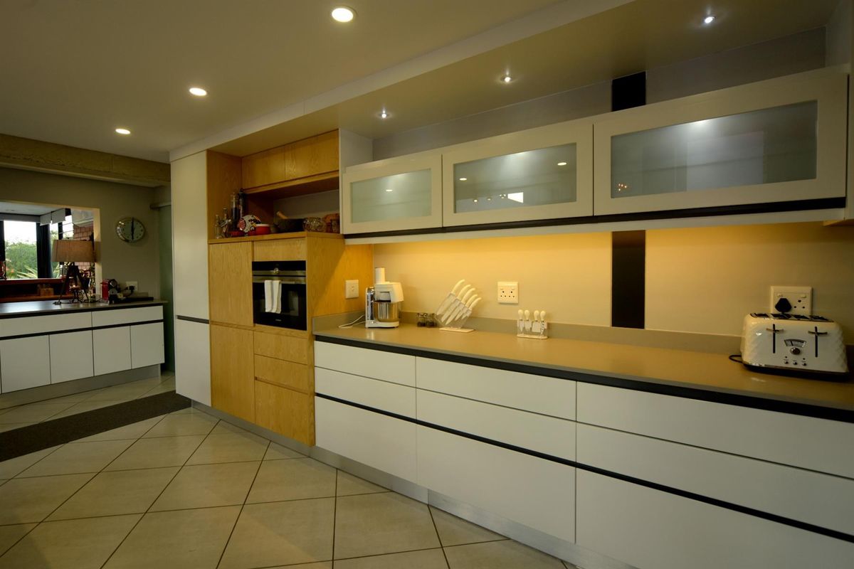 Modern kitchen featuring sleek white cabinetry, integrated oven, stone countertops, under-cabinet lighting, and recessed ceiling lights with tiled flooring.