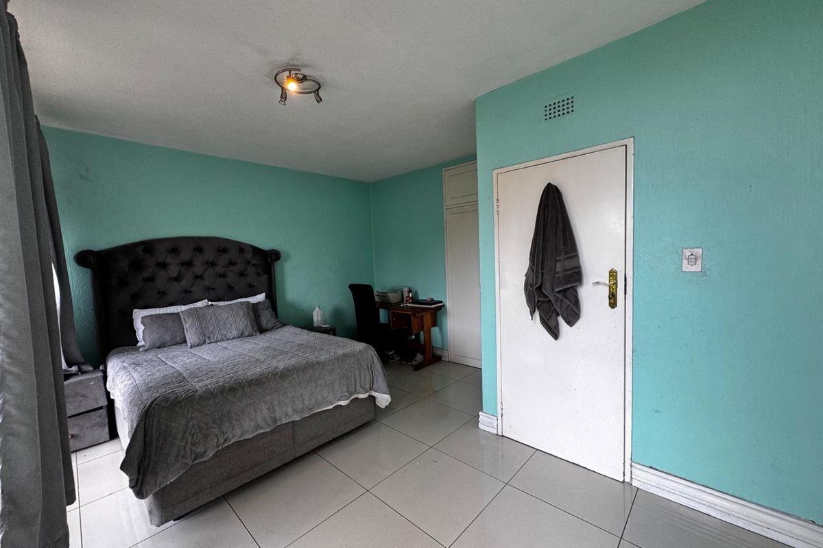 A spacious bedroom featuring tiled flooring, built-in cupboard storage, and a ceiling vent, offering a functional layout ready for personalization.