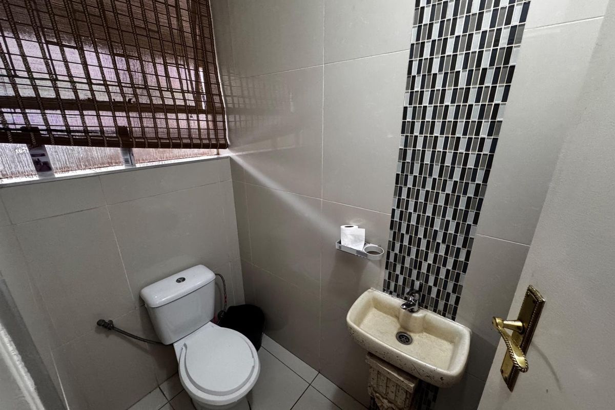 A compact guest bathroom featuring tiled walls with a decorative mosaic accent, a pedestal basin, and a standard toilet.
