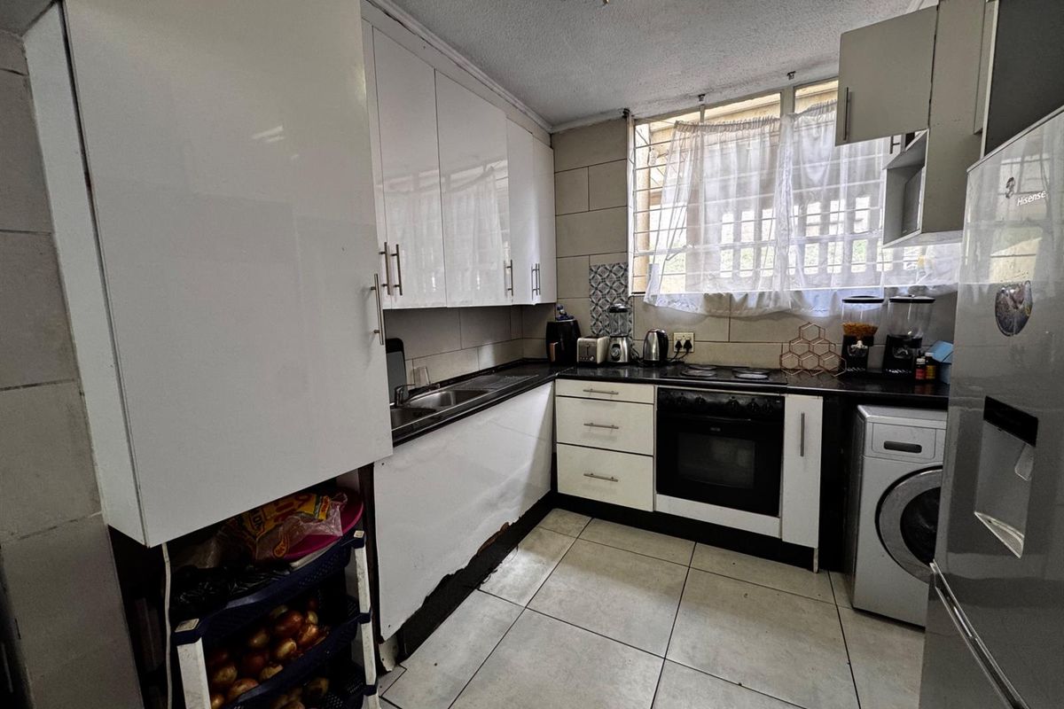 Compact kitchen featuring white cabinetry, dark countertops, built-in oven and hob, tiled flooring, and security bars on the window.
