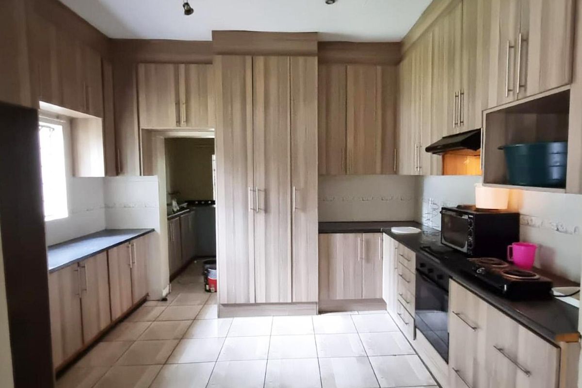 A functional kitchen featuring wood-grain cabinetry, tiled flooring, a built-in oven, and an extractor fan, with an adjacent scullery area.