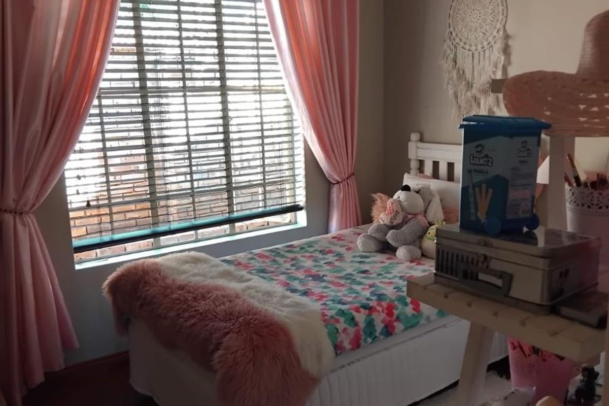 A cozy bedroom featuring laminate flooring, recessed downlights, and large windows fitted with venetian blinds and decorative curtains.