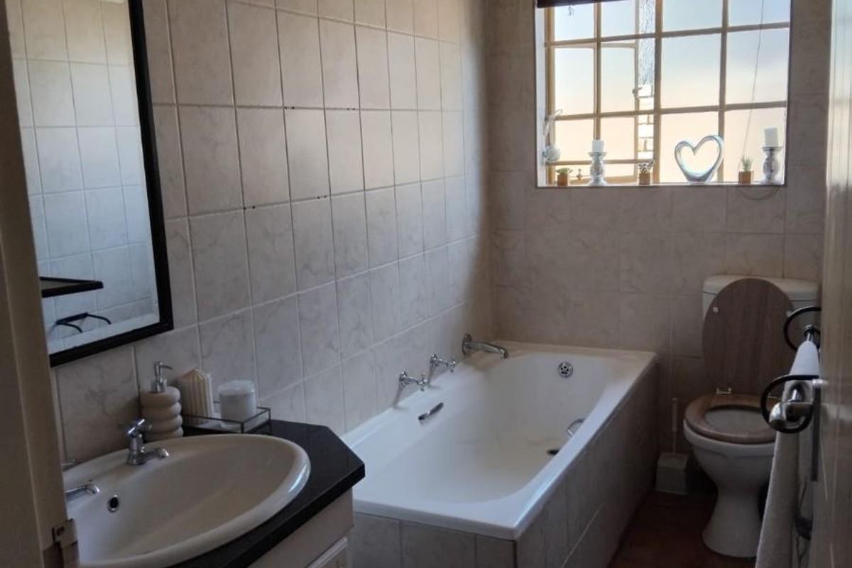 A functional bathroom featuring a built-in vanity with a basin, a standard bathtub, and a toilet, finished with neutral wall and floor tiles.