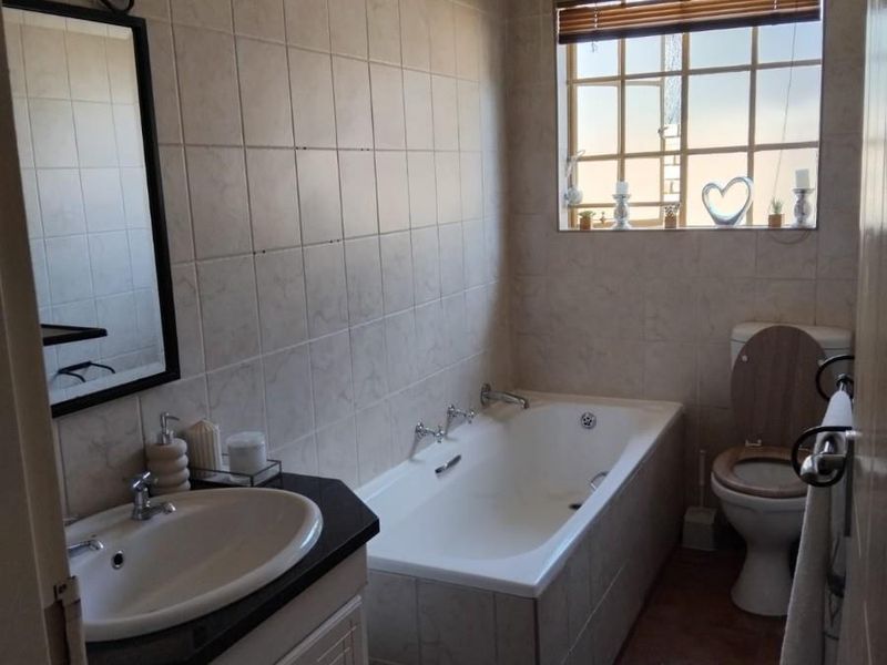 A functional bathroom featuring a built-in vanity with a basin, a standard bathtub, and a toilet, finished with neutral wall and floor tiles.