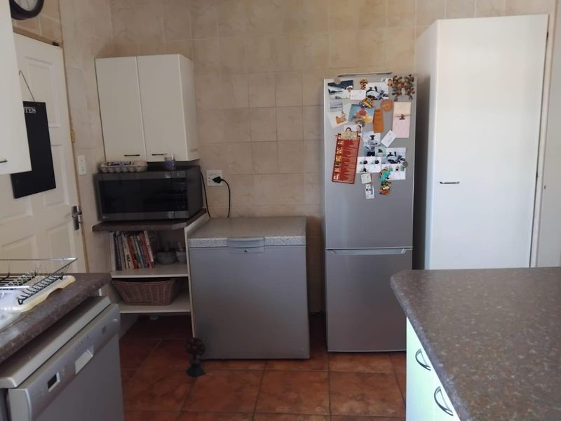 A functional kitchen area featuring tiled wall splashbacks, laminate countertops, and built-in cabinetry with tiled flooring.