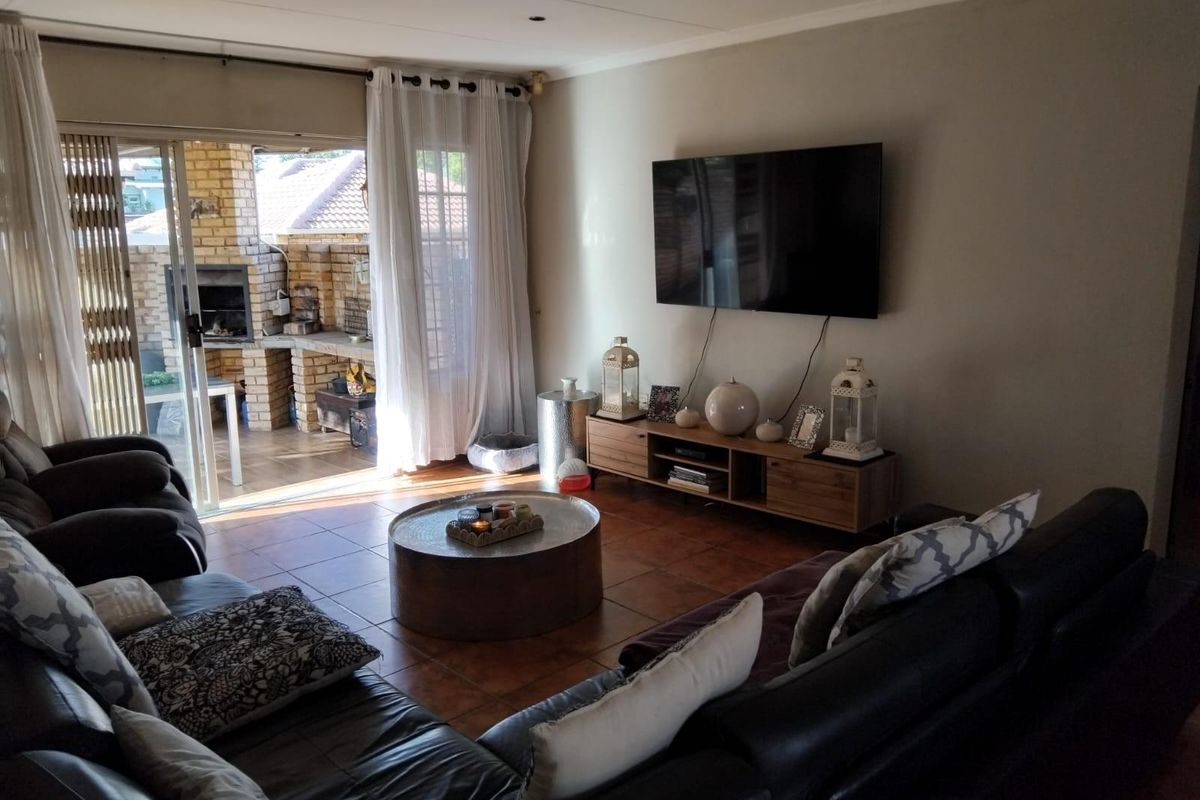 Spacious living room featuring tiled flooring and large sliding doors that open onto an outdoor patio area with a built-in brick braai.