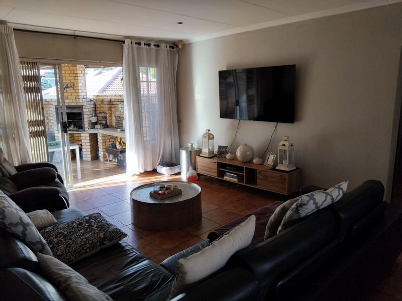 Spacious living room featuring tiled flooring and large sliding doors that open onto an outdoor patio area with a built-in brick braai.