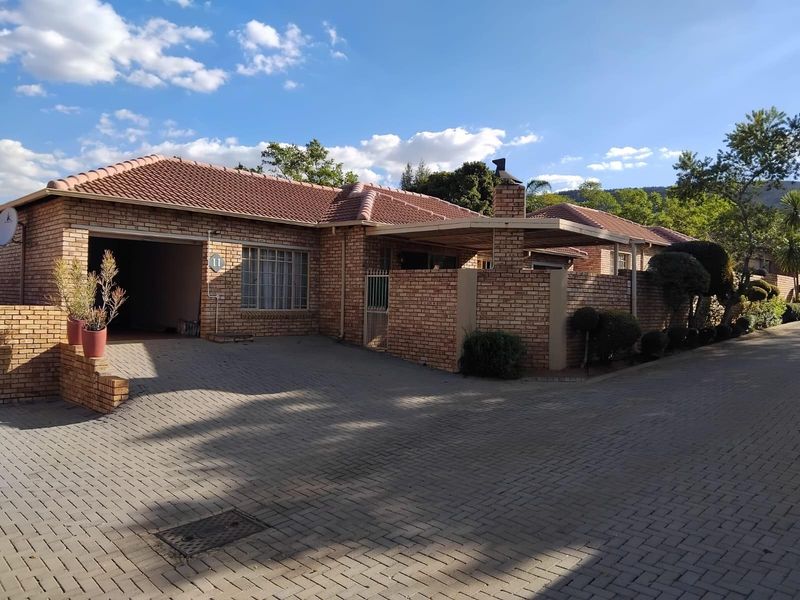 Front elevation of a brick townhouse featuring a paved driveway, integrated garage, and a covered patio area with a brick chimney.