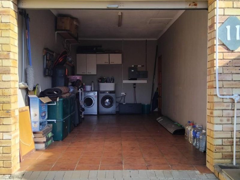 A functional garage space featuring tiled flooring, built-in storage cabinetry, and dedicated laundry plumbing connections, providing versatile utility and storage options.