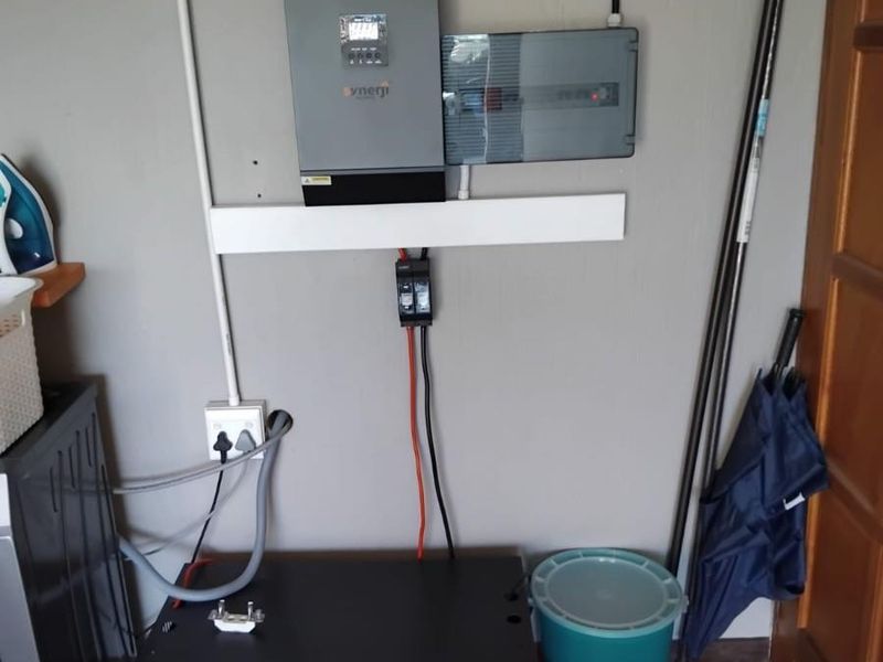 Utility area featuring a wall-mounted solar inverter, electrical distribution board, and battery storage unit for backup power.