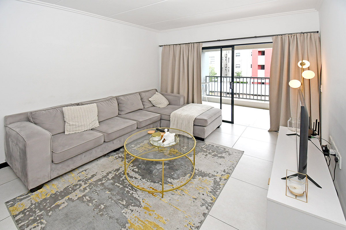 A bright and modern living room featuring large format floor tiles and a sliding glass door providing access to an outdoor balcony.