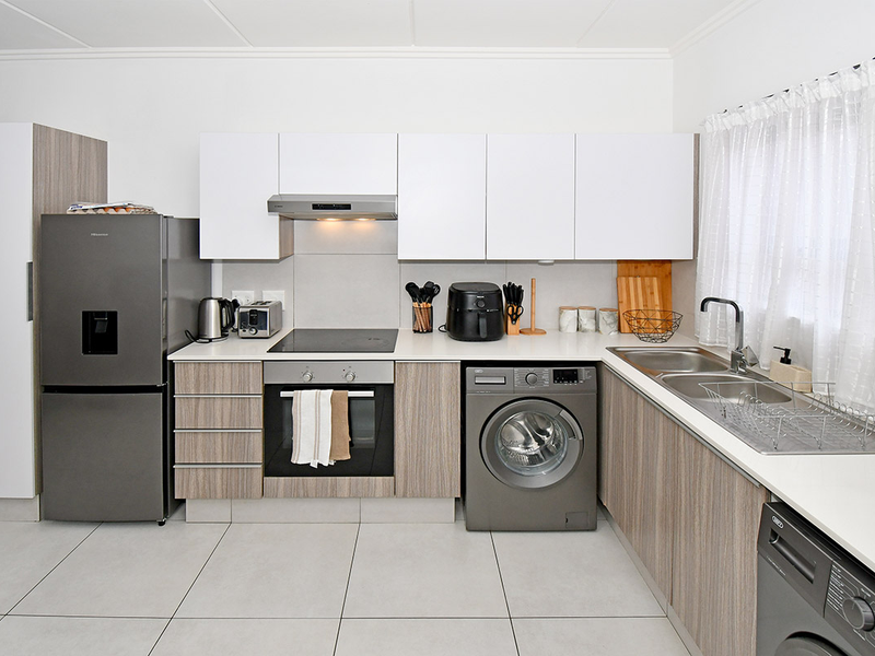 Modern kitchen featuring white and wood-grain cabinetry, integrated appliances, electric hob, oven, extractor fan, and a double sink with tiled flooring.