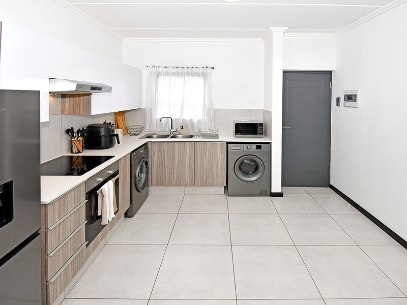 Modern kitchen featuring light wood-grain cabinetry, white upper cabinets, tiled flooring, and integrated laundry appliances, offering a clean and functional workspace.