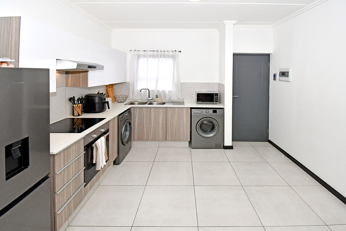 Modern kitchen featuring light wood-grain cabinetry, white upper cabinets, tiled flooring, and integrated laundry appliances, offering a clean and functional workspace.