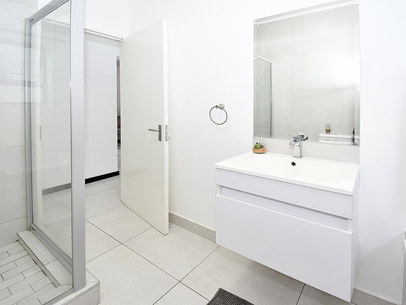 A clean, modern bathroom featuring a glass shower enclosure, a wall-mounted vanity with a basin, and neutral floor-to-ceiling tiling.