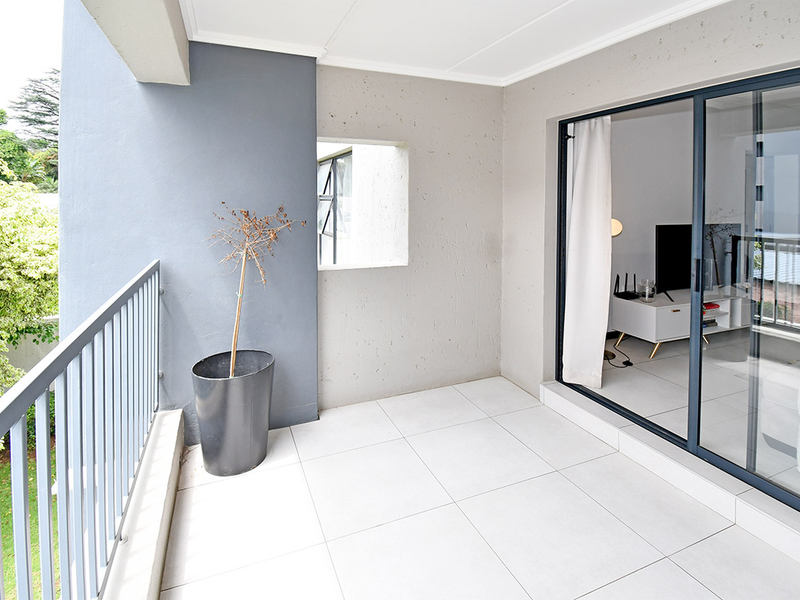 A clean, modern balcony featuring tiled flooring, a metal balustrade, and large sliding glass doors providing seamless access to the interior living space.