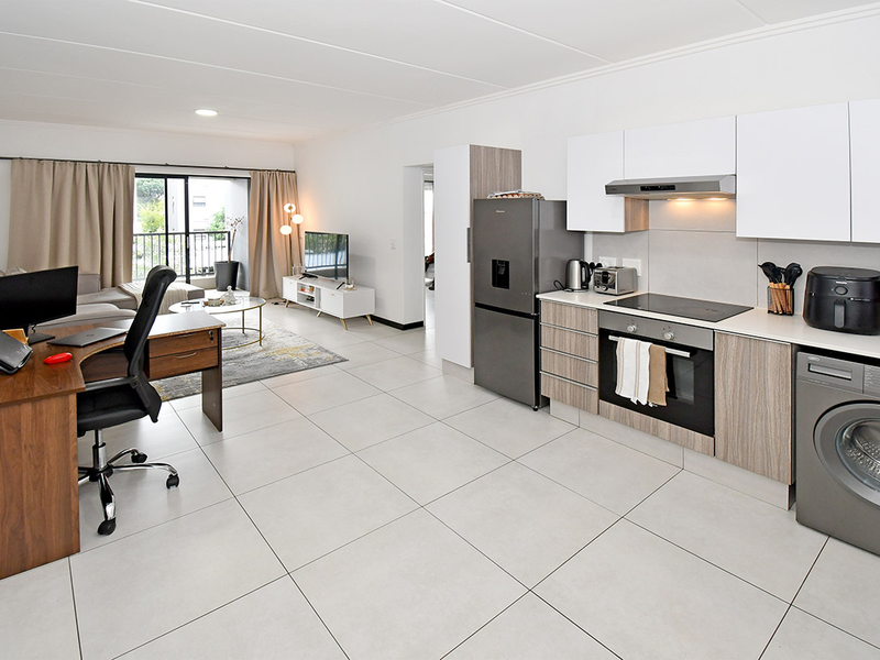 Modern open-plan living area featuring a contemporary kitchen with built-in appliances, tiled flooring, and seamless access to a private balcony.