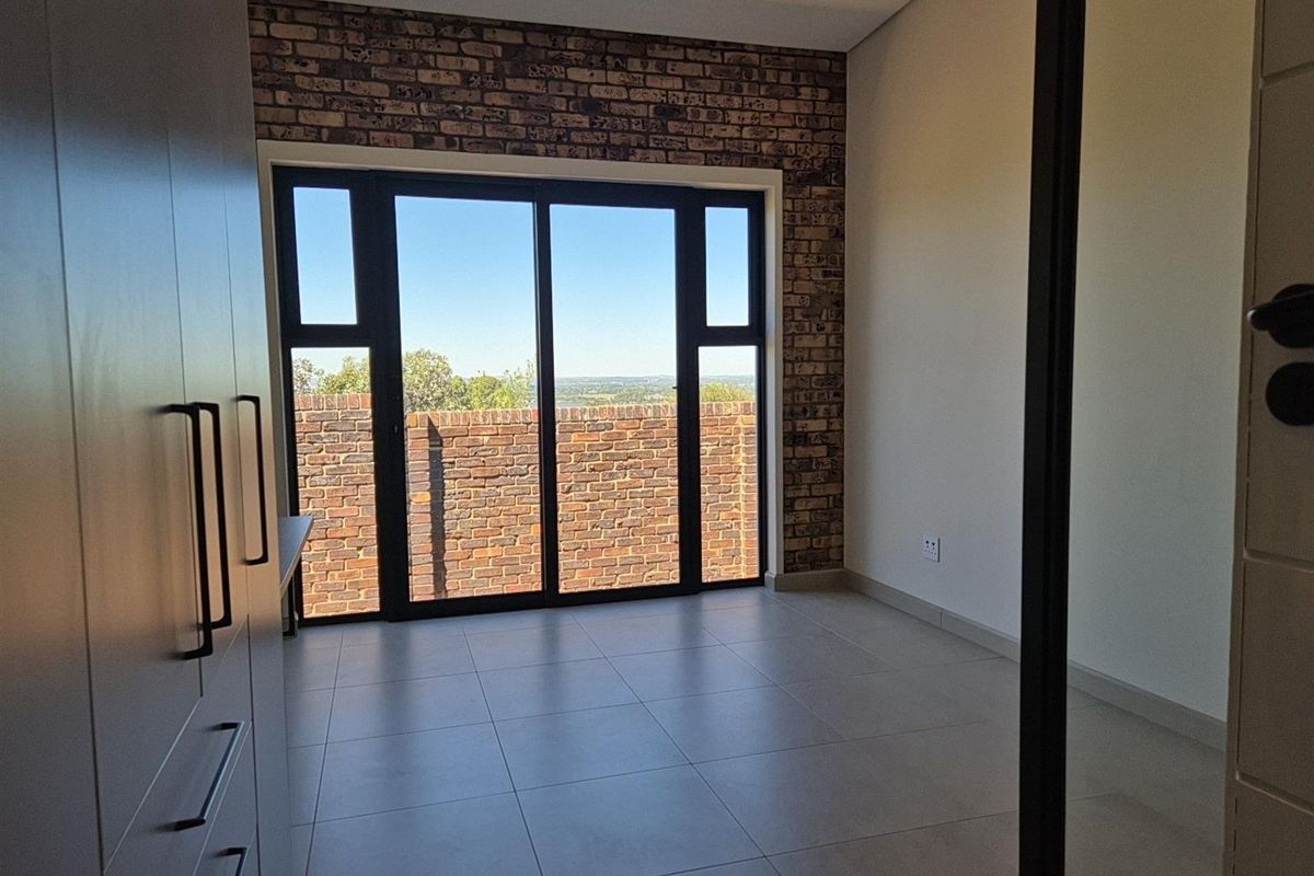 A bright bedroom featuring modern tiled flooring, a striking exposed brick feature wall, and large sliding glass doors opening to an outdoor view.