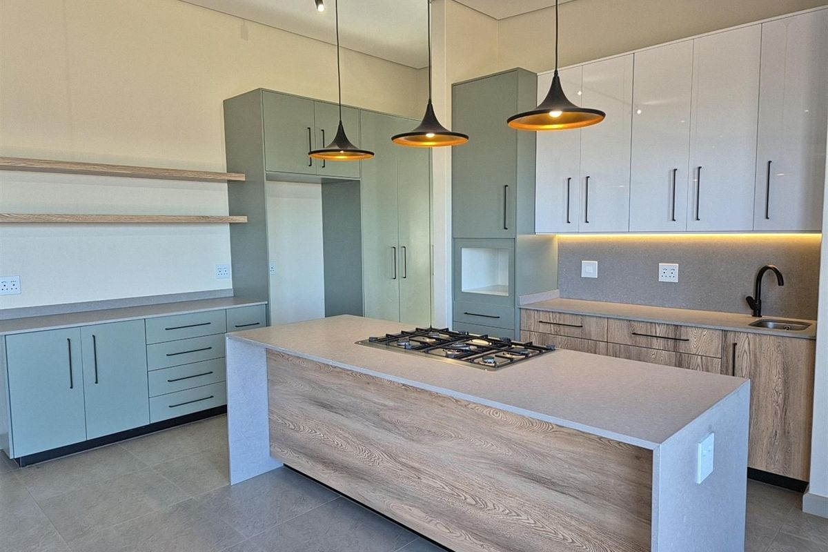 Modern kitchen featuring a central island with a built-in gas hob, sleek cabinetry, stone countertops, and contemporary pendant lighting.