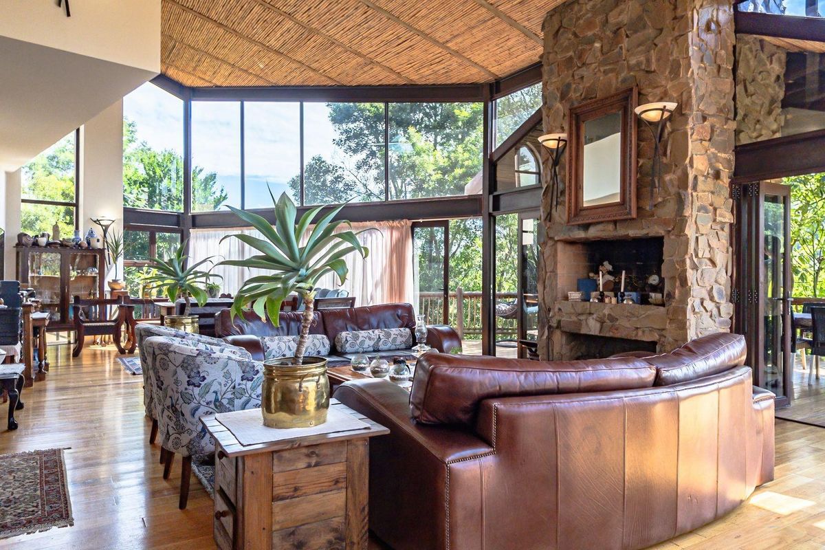Spacious living area featuring a prominent stone fireplace, high thatched ceiling, and expansive floor-to-ceiling windows offering abundant natural light and garden views.