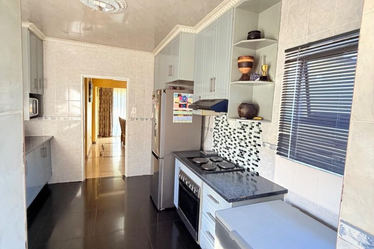 A functional kitchen featuring dark tiled flooring, built-in cabinetry, a fitted stove with extractor fan, and tiled wall finishes.