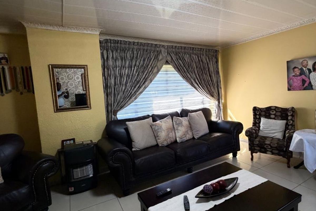 A comfortable living room featuring tiled flooring, a central ceiling light fixture, and large windows with decorative curtains.