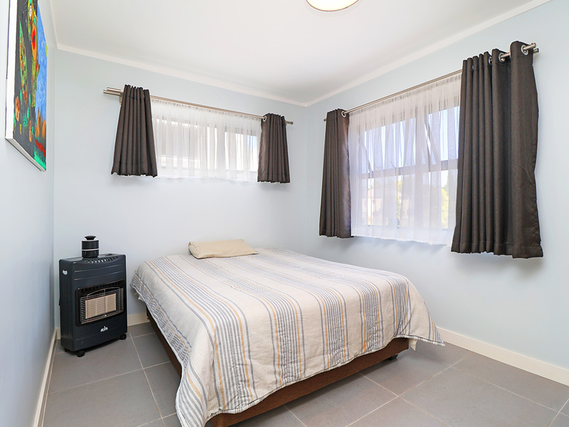 A functional bedroom featuring tiled flooring, dual windows with curtain rods, and neutral wall finishes.