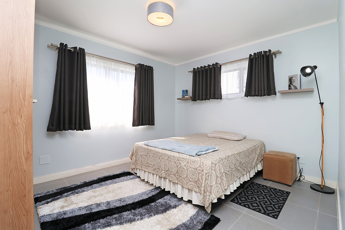 A well-maintained bedroom featuring neutral tiled flooring, built-in storage, and dual windows with curtain rods, offering a clean and functional living space.
