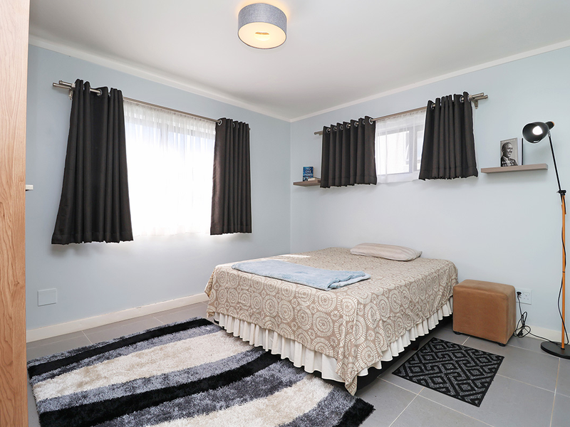 A well-maintained bedroom featuring neutral tiled flooring, built-in storage, and dual windows with curtain rods, offering a clean and functional living space.