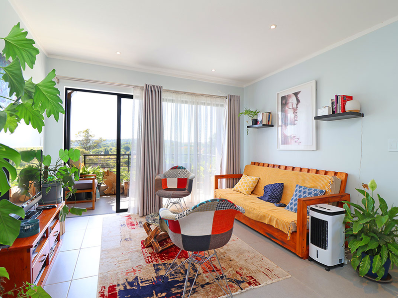 A bright and well-maintained living room featuring tiled floors, recessed lighting, and a large sliding glass door providing access to the balcony.