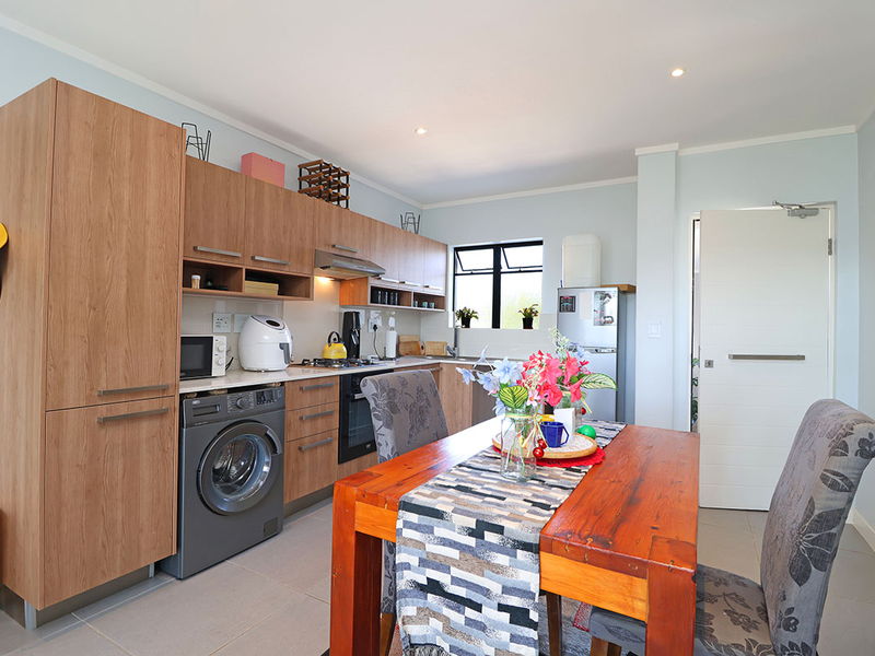 Modern open-plan kitchen featuring wood-finish cabinetry, integrated appliances, and tiled flooring, seamlessly flowing into the dining area.