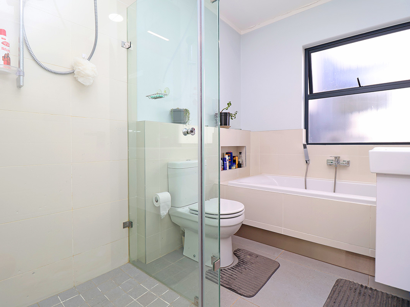 A functional bathroom featuring a glass-enclosed shower, a built-in bathtub, a toilet, and a vanity basin with neutral wall and floor tiling.
