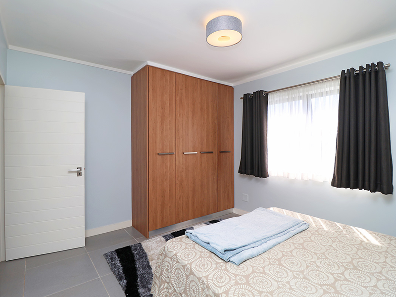 A well-maintained bedroom featuring neutral wall tones, tiled flooring, and a large built-in wooden wardrobe.