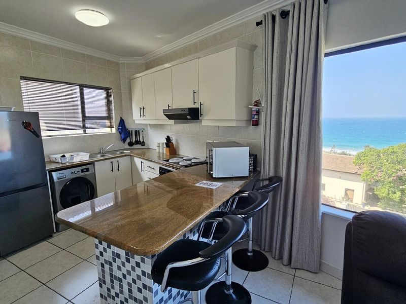 Open-plan kitchen featuring granite countertops, built-in cabinetry, and a breakfast bar, with large windows offering scenic ocean views.