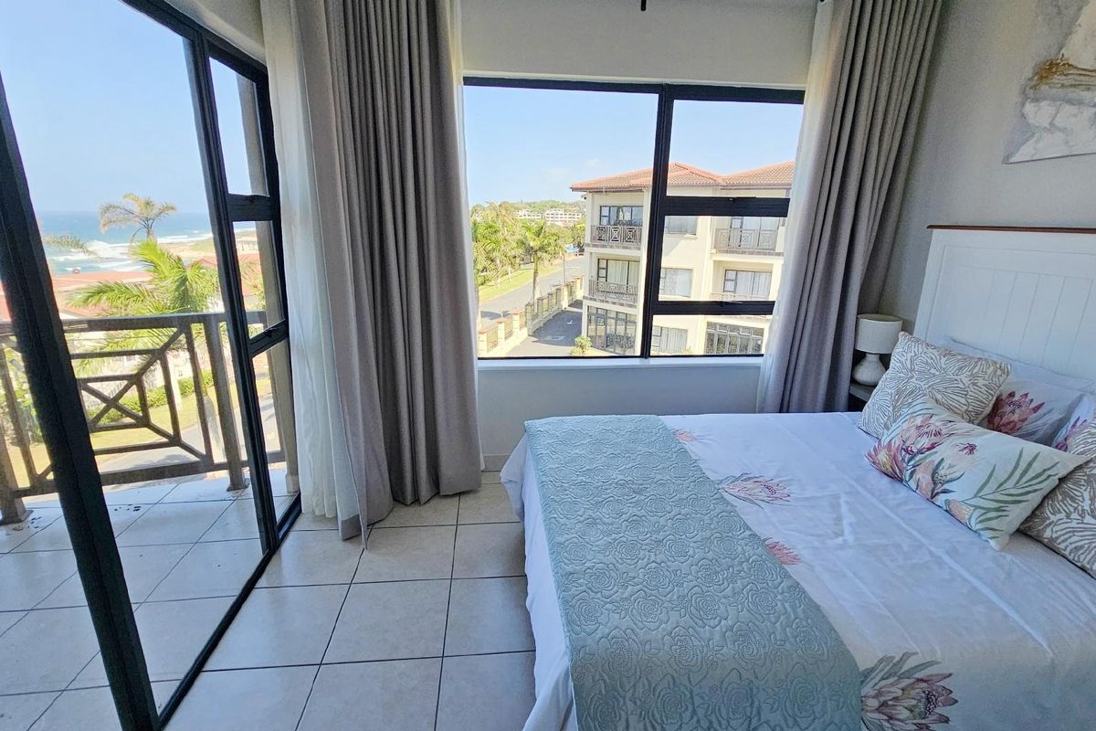 Bright bedroom featuring large windows and sliding glass doors that open onto a private balcony with scenic coastal and neighbourhood views.