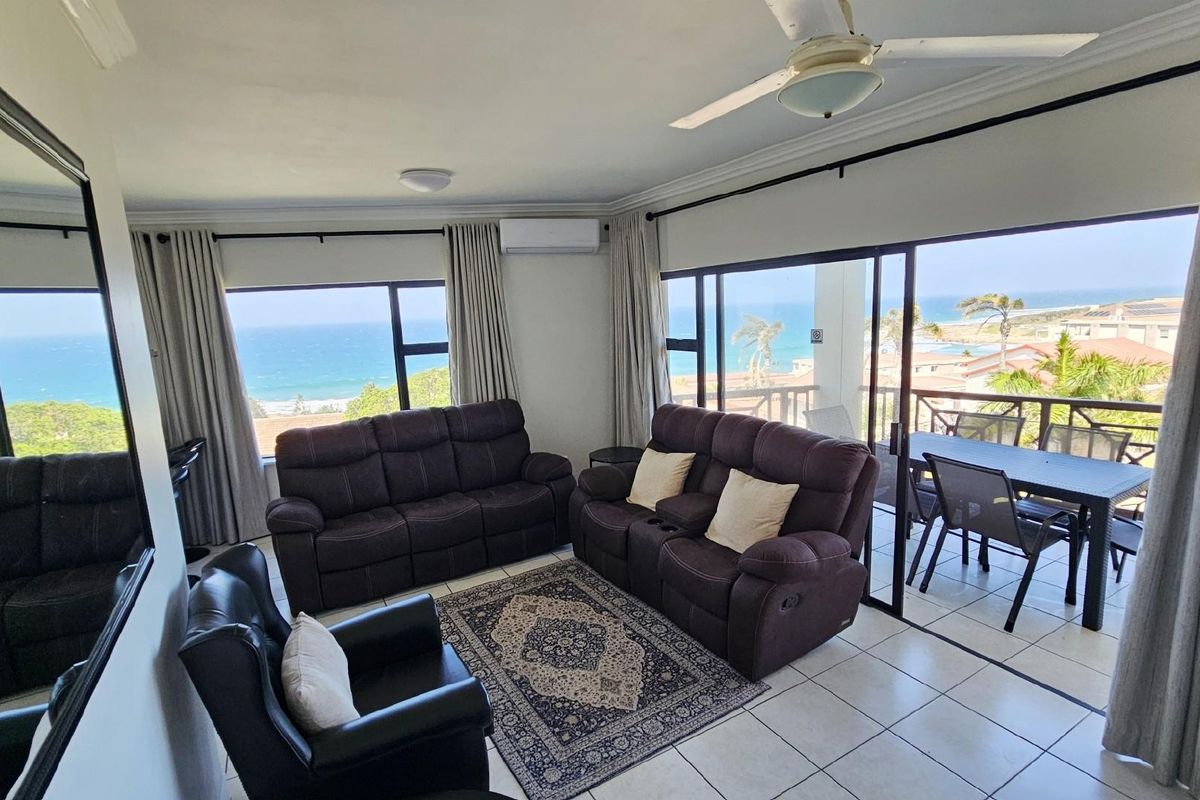Spacious living area featuring large windows and sliding doors that open to a balcony with panoramic ocean views.