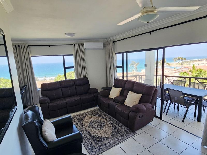 Spacious living area featuring large windows and sliding doors that open to a balcony with panoramic ocean views.