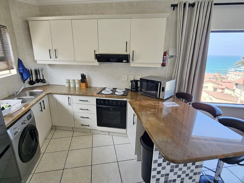 Compact kitchen featuring granite countertops, built-in oven and hob, extractor fan, and tiled flooring, with an integrated breakfast bar and ocean views.