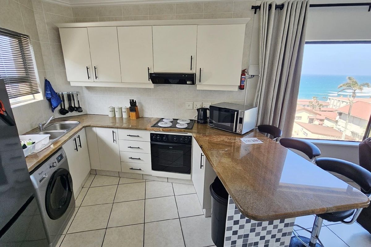 Compact kitchen featuring granite countertops, built-in oven and hob, extractor fan, and tiled flooring, with an integrated breakfast bar and ocean views.
