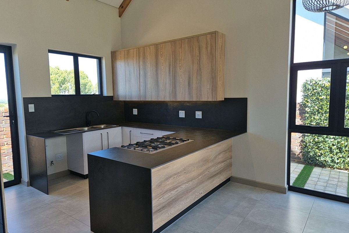 Modern kitchen featuring wood-grain cabinetry, dark stone countertops, a built-in gas hob, and large windows providing ample natural light.
