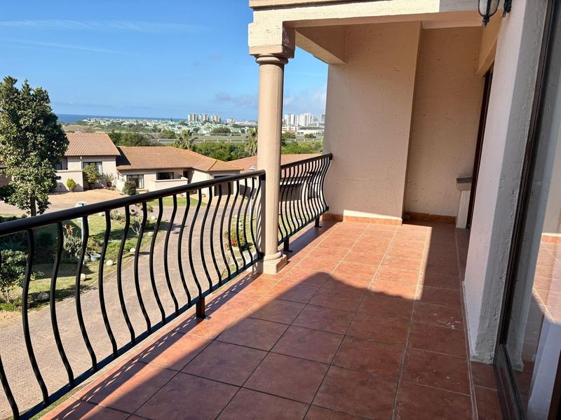 A spacious covered balcony featuring tiled flooring, a decorative wrought iron balustrade, and a concrete column, offering elevated views of the surrounding estate.