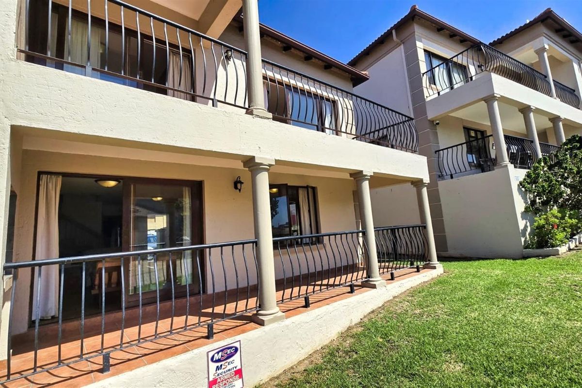 A view of the townhouse exterior featuring a covered ground-floor patio and an upper-level balcony with decorative metal railings and structural columns.