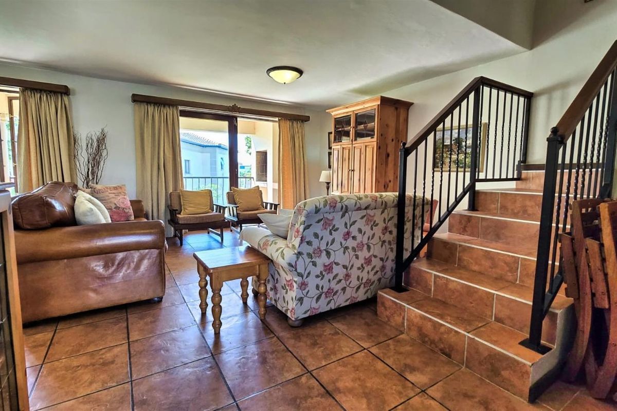 Spacious living area featuring terracotta floor tiles, a staircase with metal balustrades, and sliding glass doors leading to an outdoor balcony.