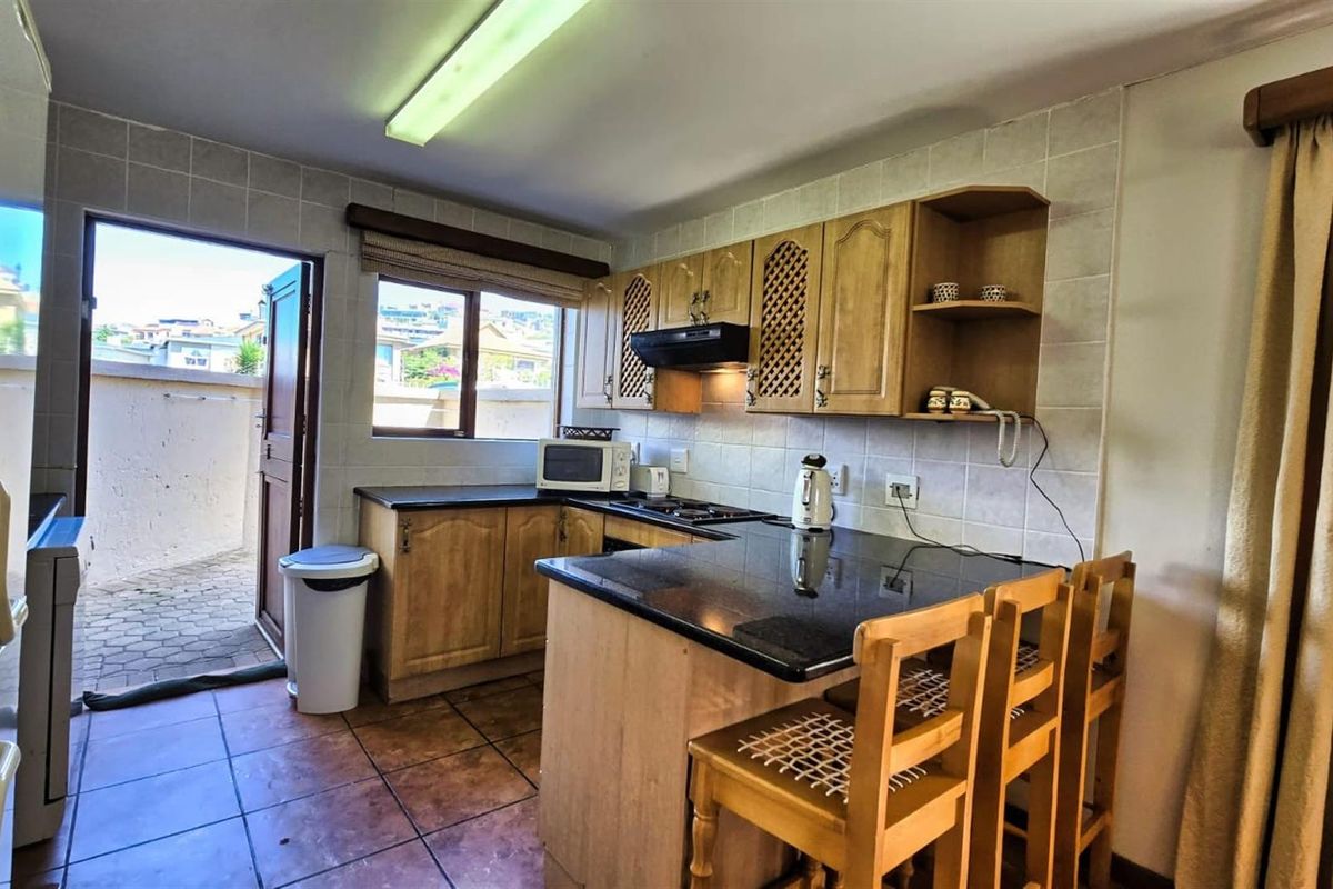 A functional kitchen featuring wooden cabinetry, dark granite countertops, a breakfast nook, and direct access to an outdoor paved area.