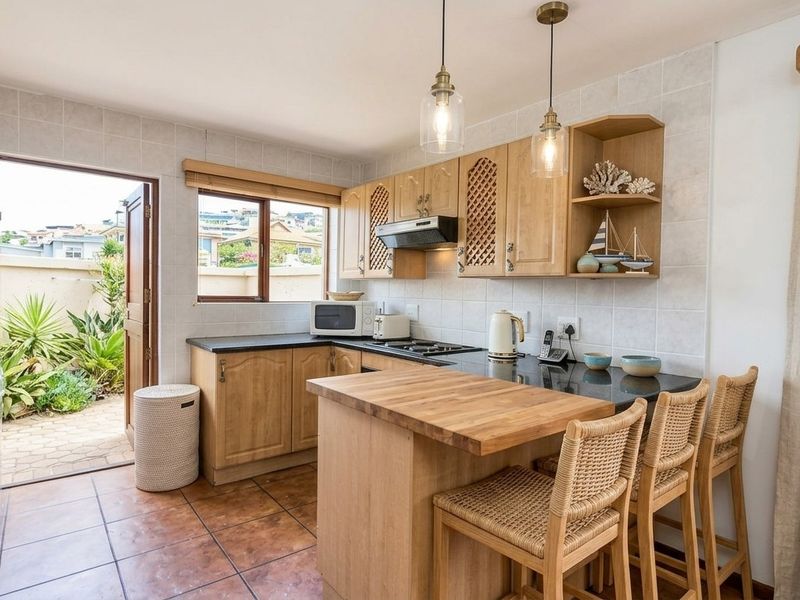 A functional kitchen featuring wooden cabinetry, granite countertops, a breakfast bar, and direct access to a private outdoor patio area.